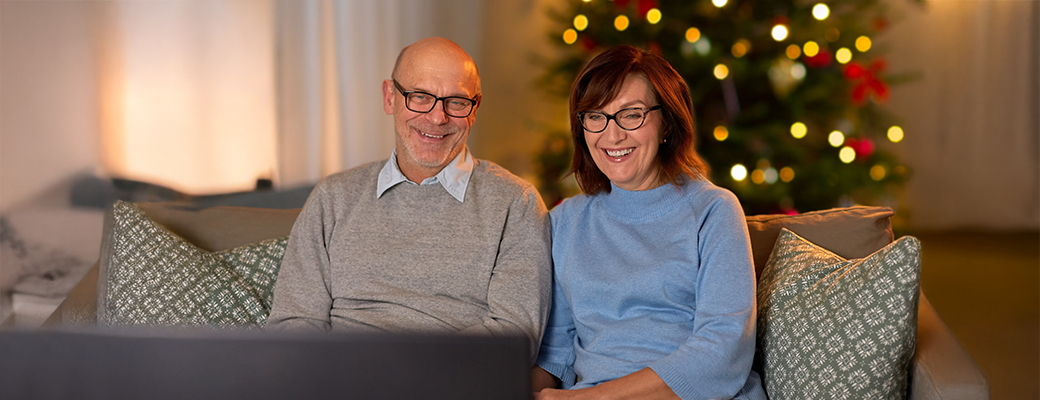 Image of middle-aged man and woman sitting on couch and watching a holiday movie